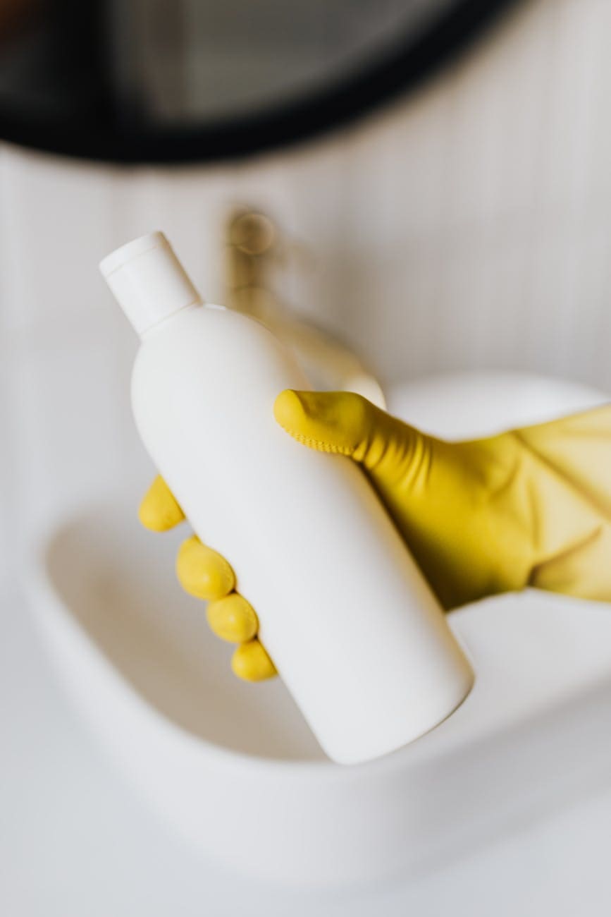 crop person in rubber gloves with white cosmetic bottle